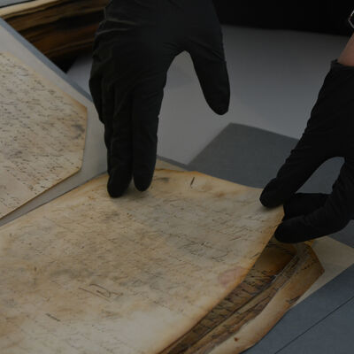 Bild vergrößern: Ein Archivale wird schonend mit handschuhtragenden Händen umgeblättert