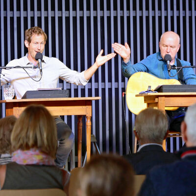 Bild vergrößern: Zwei Männer auf der Bühne sitzend mit Mikrofonen und Gitarre