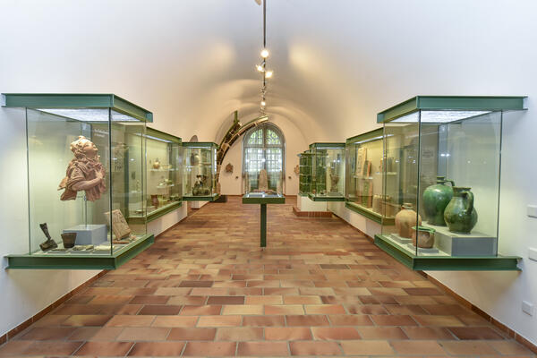 Bild vergrößern: Ausstellungsraum im Stadtmuseum mit Vitrinen links und rechts sowie einer zentrierten Vitrine